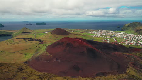 Vista-Escénica-De-La-Naturaleza-Con-Estuario-Volcánico-En-Prados-Y-Paisaje-Urbano-Al-Fondo-En-Westman,-Sur-De-Islandia