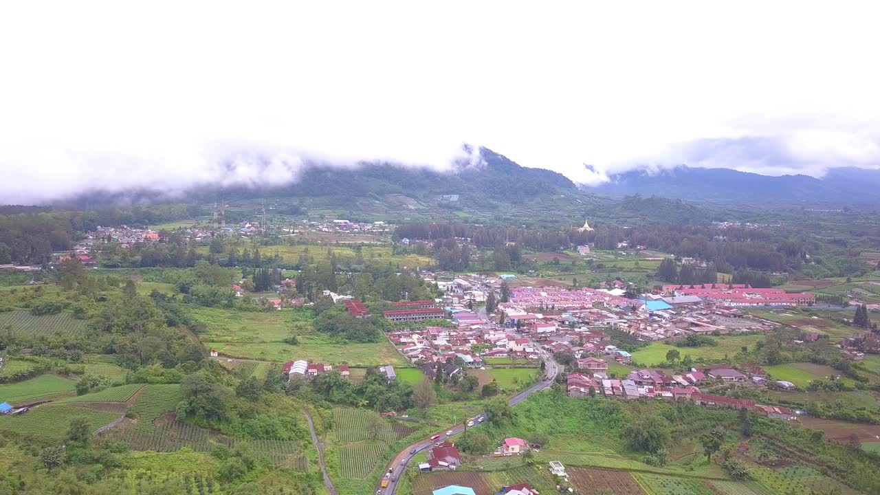 vista aérea de vuelo hacia adelante de un hermoso pueblo con campo verde y montañas cubiertas por las nubes