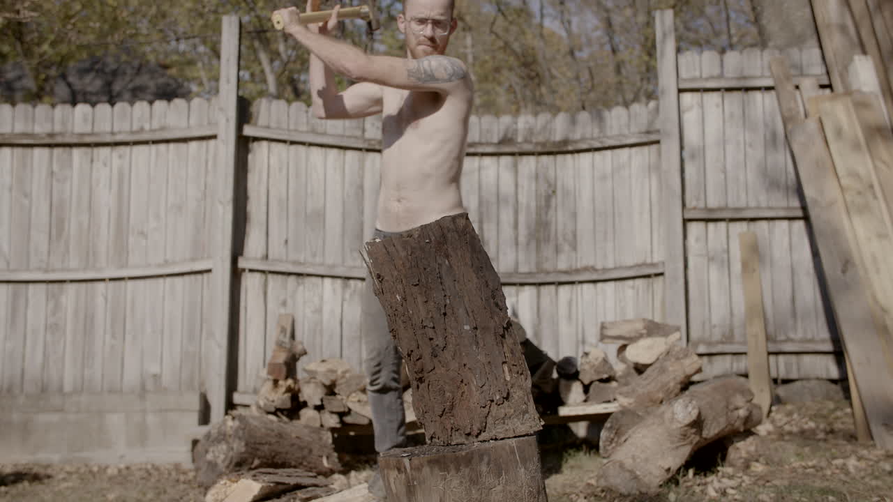 Slow motion front on wide angle of man without shirt on splitting a log with a axe