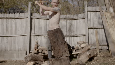 slow motion front on wide angle of man without shirt on splitting a log with a axe