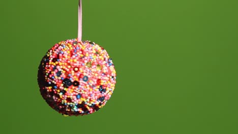 ornament covered in sequins spinning on a white ribbon in front of a green screen