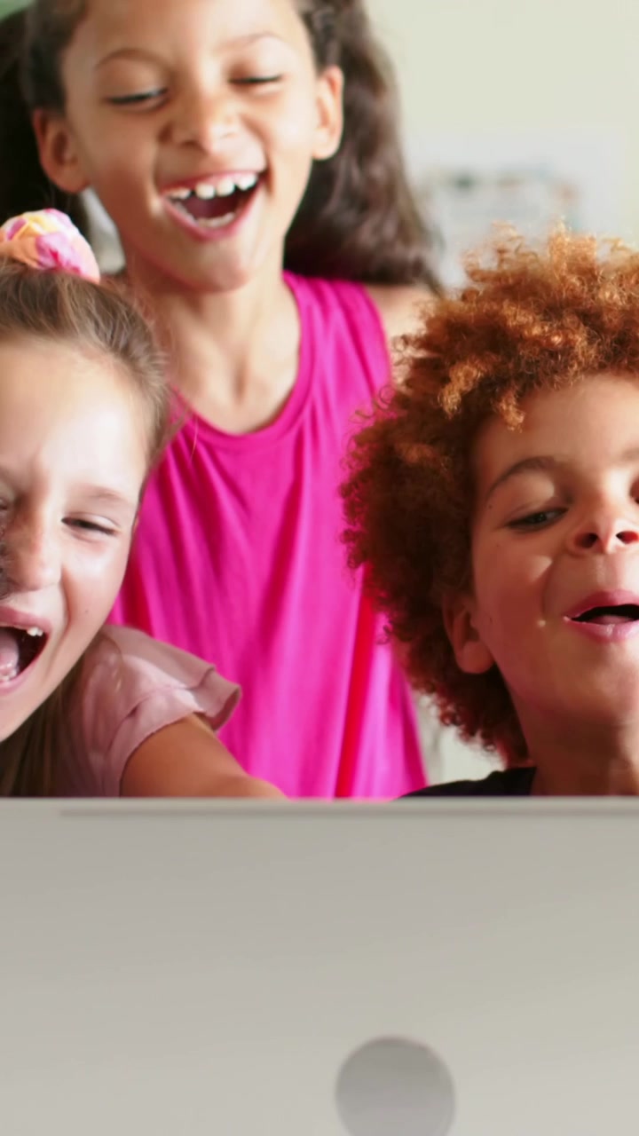 Vertical video: Reacting kids crowding around laptop at home, girl in bright pink pointing at clip