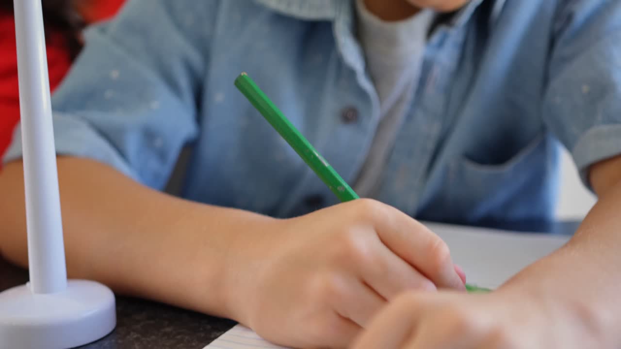 vista frontal de un escolar caucásico estudiando en el escritorio en el aula 4k