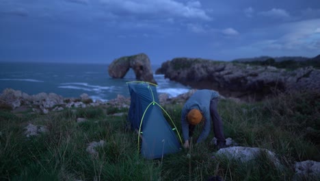 Camping-man-assembling-and-pitching-tent-at-remote-nature-ocean-cliff