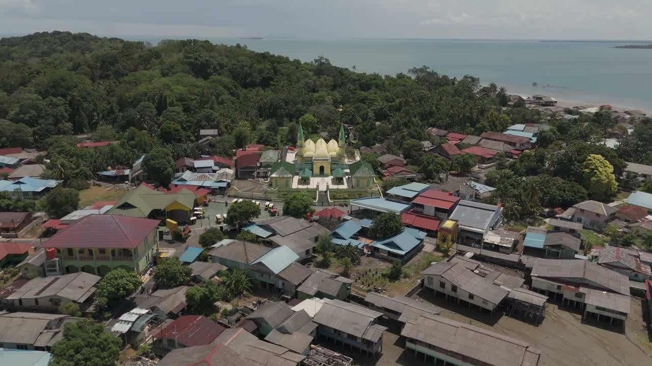 Aerial drone view pushing in on the beautiful Sultan Riau Grand Mosque (Masjid Sultan Riau) surrounded by a traditional village and tropical forest on Penyengat Island, Riau Islands, Indonesia
