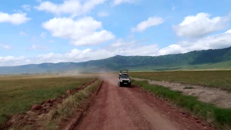 Zwei-Fahrzeuge,-Die-Im-Ngorongoro-krater-Mit-Staubigen-Straßen-Und-Berglandschaft-Vorbeifahren