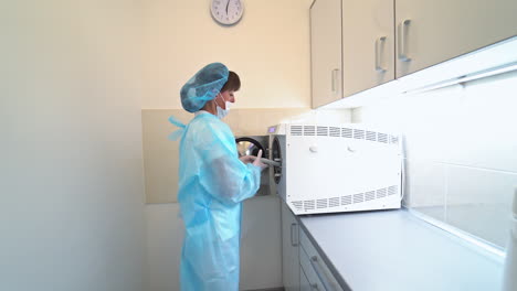 woman in mask presses buttons on the sterilizer. nurse is taking the dentistry tools off the sterilizing machine for usage.