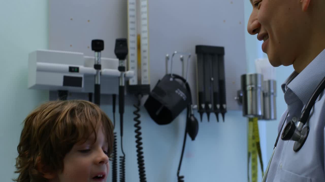 젊은 아시아 남성 의사가 클리닉 4k에서 백인 소년 환자에게 심장 모델을 보여주는 측면 뷰