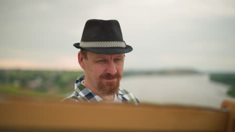 a craftsman, dressed in a checkered shirt and black hat, is deeply engrossed in painting on a board in the middle of a green field. his serious expression highlights his concentration