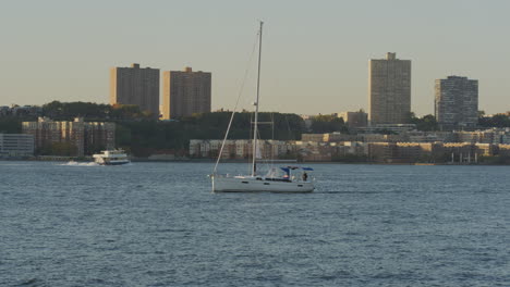 sailboat with single mast navigating along calm waters of the hudson river with new jersey seen in background