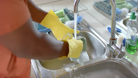 mid section of african american man washing dishes in bright kitchen, slow motion