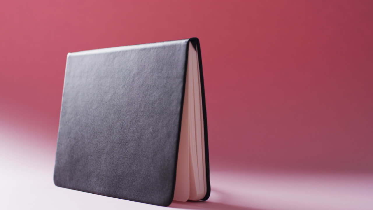 Close up of open black book standing horizontal with copy space on red background in slow motion