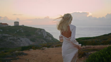 blonde woman moving castle seashore vertical back view. happy girl run valley