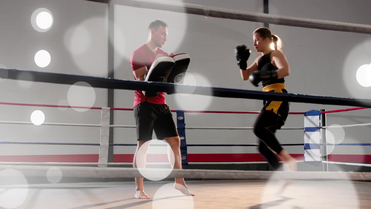 Coach moving pads, athlete throwing jabs, circling, front kicking, boxing training ring with bokeh