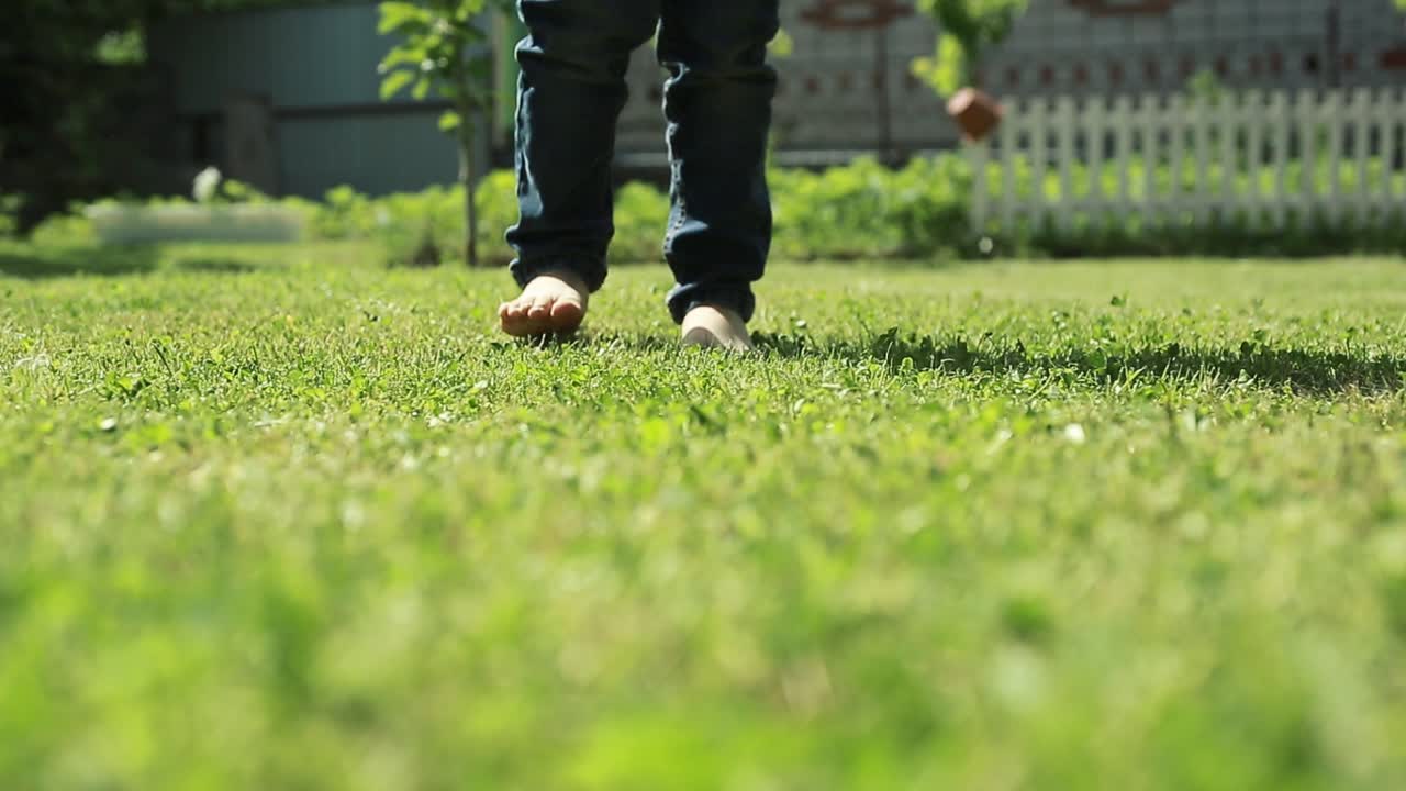 Happy Kid Jumping In Green Field. Summer vacation concept, barefoot boy on summer green grass