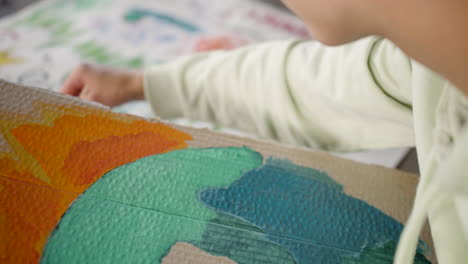 Close-up-of-unrecognizable-environmental-activist-painting-placards-sitting-on-the-floor