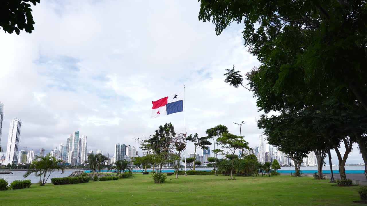Panama's national flag waving the wind, at a park, against modern tall buildings and skyscrapers near the coastline