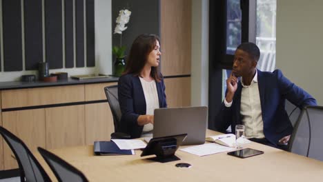 Diverse-businessman-and-businesswoman-discussing-and-using-laptop-in-modern-office