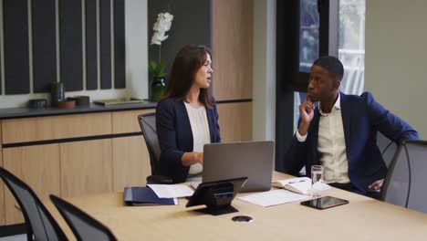 diverse businessman and businesswoman discussing and using laptop in modern office