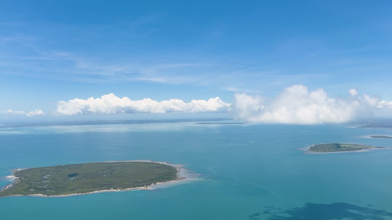 Smooth aerial flight above tropical islands, turquoise ocean water, distant coastline, and bright clouds