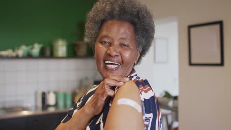 happy senior african american senior woman showing plaster on arm after covid vaccination