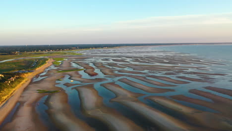 cape cod bay aerial drone footage of beach at low tide during golden hour, bright sun low and setting, pan right