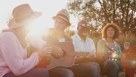 Grupo-De-Amigos-Maduros-Sentados-Alrededor-Del-Fuego-Mientras-Beben-Y-Cantan-Canciones-En-Un-Campamento-Al-Aire-Libre