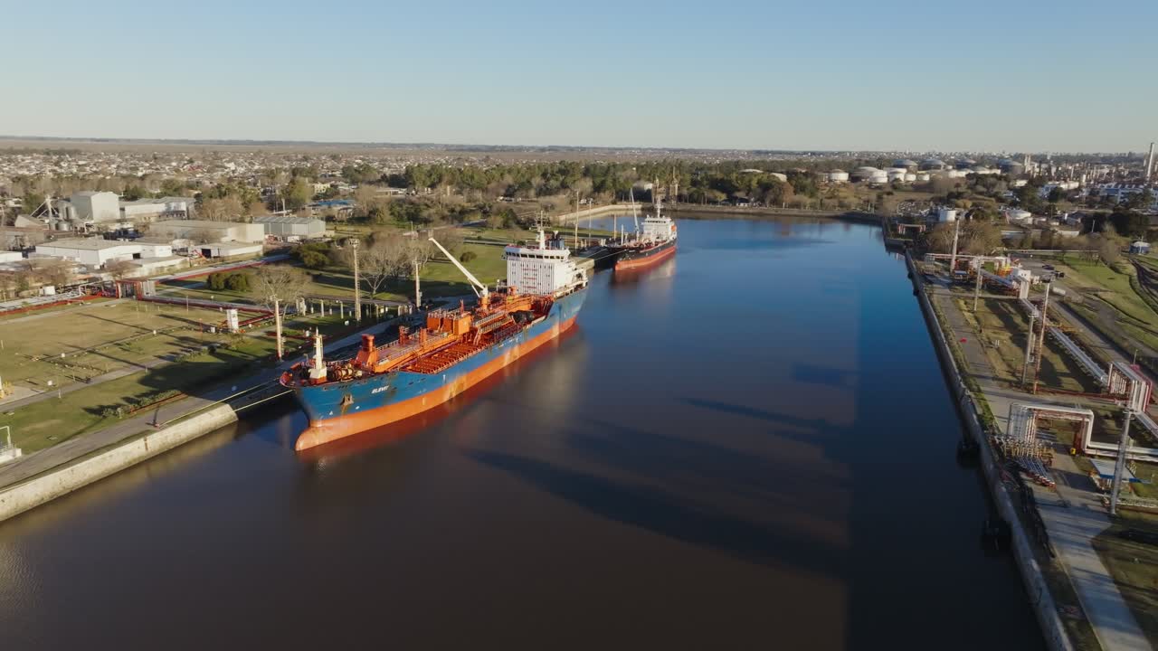 Aerial drone footage showing a cargo vessel moored at a river port with shipping infrastructure and daytime activity