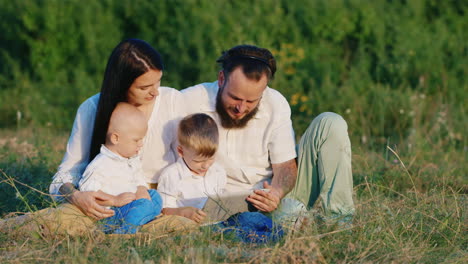 dos hermanos pequeños con sus padres juegan en una tableta entre el prado florido