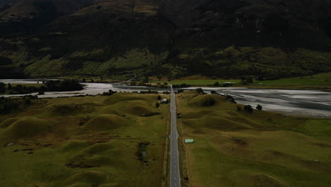 Beautiful-road-bridge-over-river-near-mountain-ranges-in-New-Zealand,-aerial-view