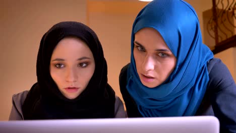 closeup portrait of two young muslim businesswomen in hijabs discussing the data in front of the laptop. boss instructing a female employee.