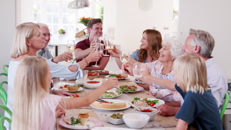 Toma-En-Cámara-Lenta-De-Una-Familia-Multigeneracional-Sentada-Alrededor-De-La-Mesa-Y-Haciendo-Tostadas-Antes-De-Disfrutar-De-La-Comida-Juntos