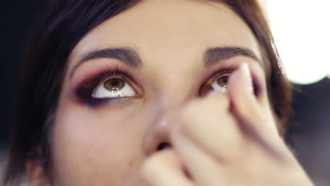 adding some gold pigmented eyeshadow in inner corner of beautiful brunette girl's eyes. creating flawless colorful smokey make up look. make up artist craft.