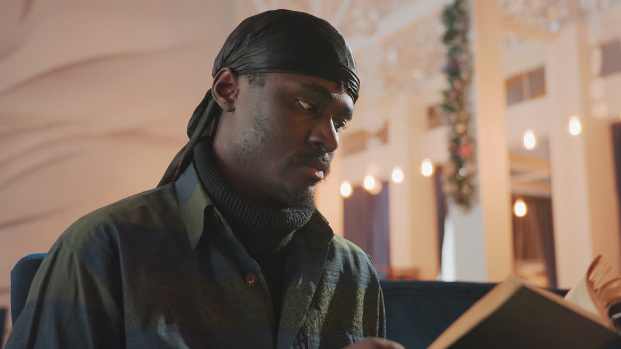 En person, der læser afslappet i et blødt lysskær, en person fordybet i en bog med en levende sløret baggrund, en afslappet klædt mand, der fokuserer på læsning med omgivende belysning og en refleksiv stemning