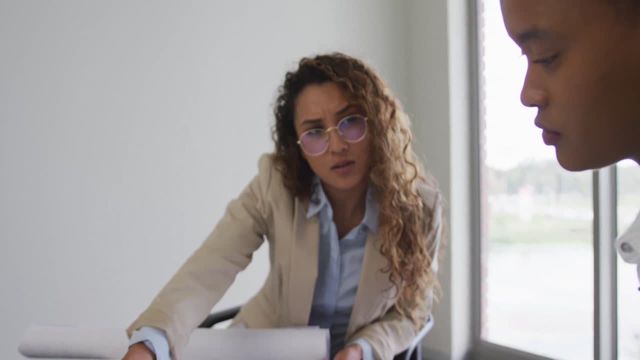 arquitectas biraciales hablando y comprobando planes de arquitectos en oficinas modernas