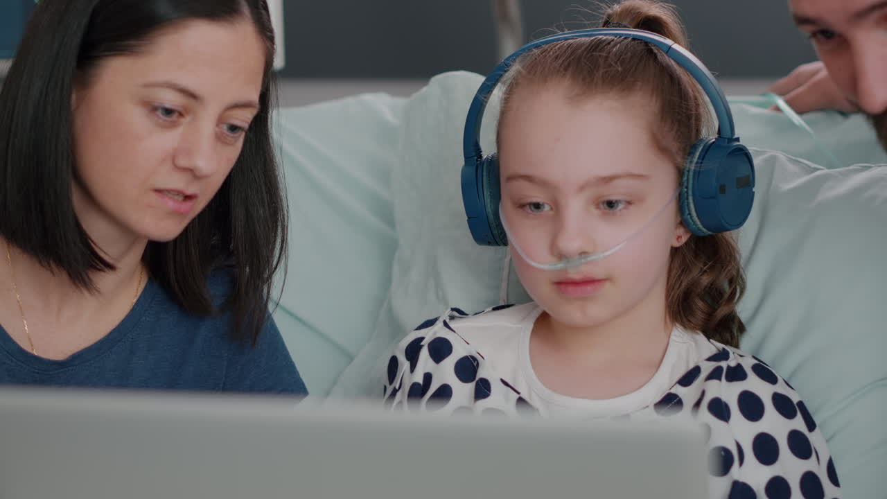 Family sitting beside daughter while playing online videogames using laptop computer in hospital ward