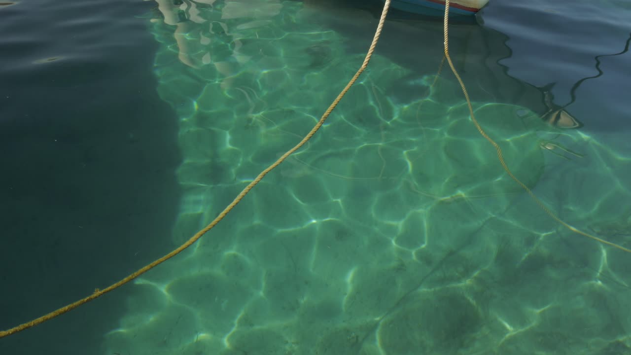 Primo piano del riflesso della luce solare nel mare cristallino verde vicino a una piccola barca da pesca ancorata nel porto di Egliali in Grecia