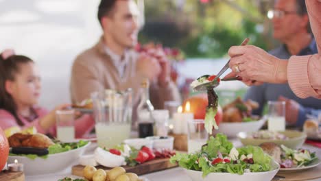 Video-of-happy-caucasian-parents,-daughter-and-grandparents-serving-food-at-outdoor-table