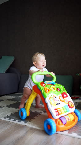 happy caucasian blond baby pushing a stroller learning to walk. adorable kid laughing sweetly. vertical video.