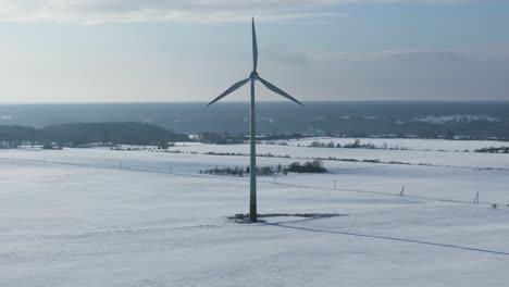 wind turbine in a snowy landscape with distant trees and fields