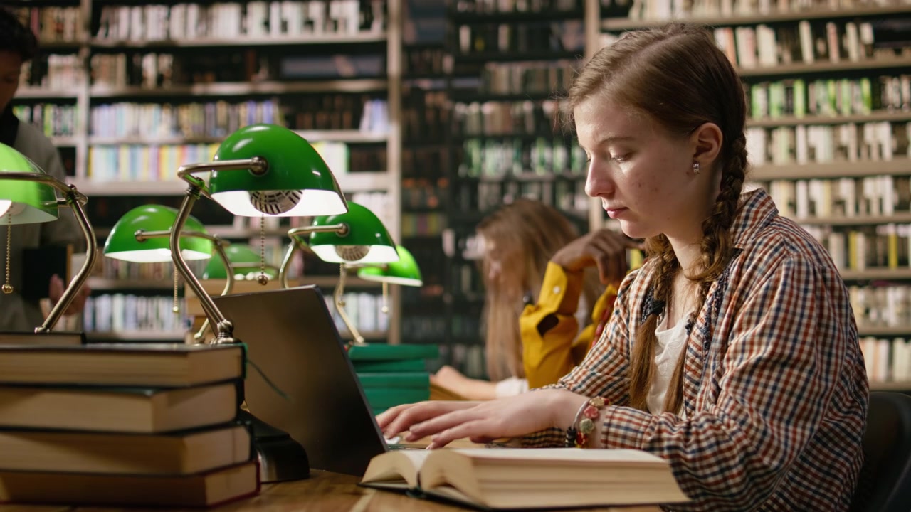 Woman learner studying at shared library table with laptop and open book