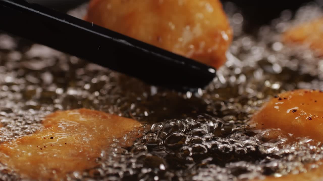American chiken nuggets broiling on black frying pan close-up macro. Breaded nagget of chiken meat. Man cooking fast food. High quality 4k footage
