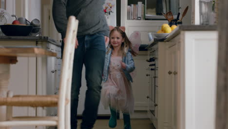 Niña-Feliz-Persiguiendo-A-Su-Padre-En-La-Cocina-Jugando-Con-Un-Lindo-Disfraz-De-Hada-Disfrutando-De-Diversión-En-Casa-Con-Papá