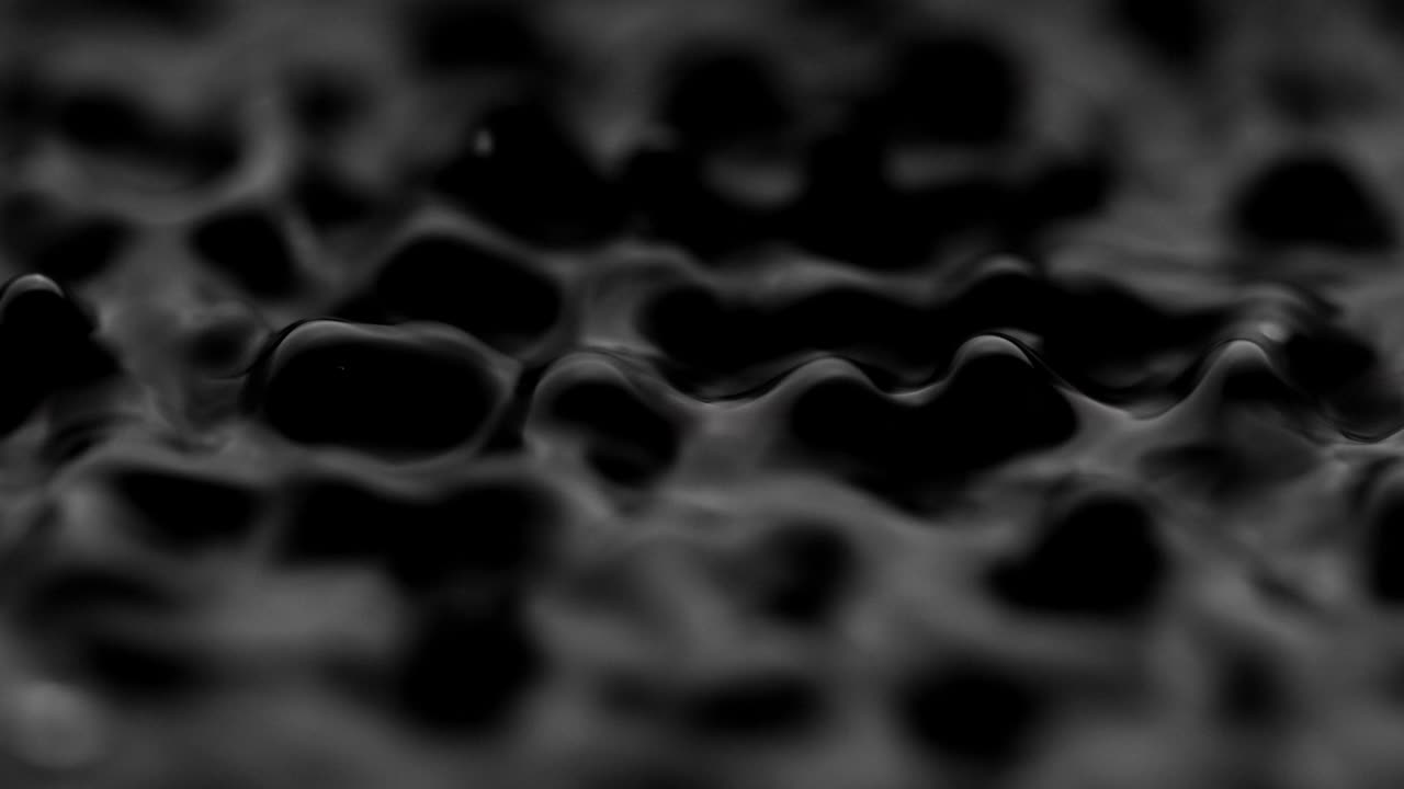 Schizzi e gocce sulla superficie del liquido. Sfondo nero astratto. Vibrazione dell'acqua. 4K slow motion 100 fps, ProRes 422, 10 bit.