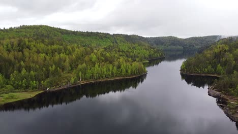 Experience-the-peaceful-reflections-of-Løvdalsvannet-Lake-from-above,-surrounded-by-Norway's-lush-greenery