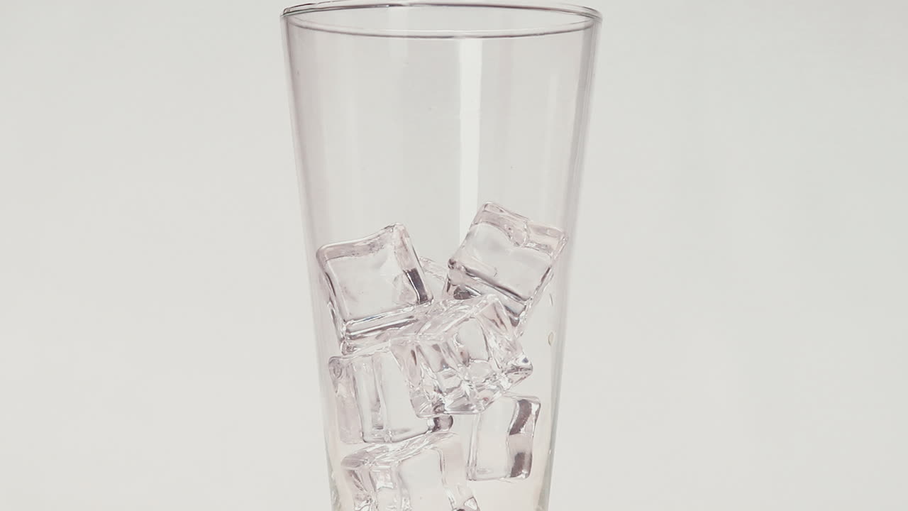 los cubos de hielo caen en un vidrio transparente de fondo blanco