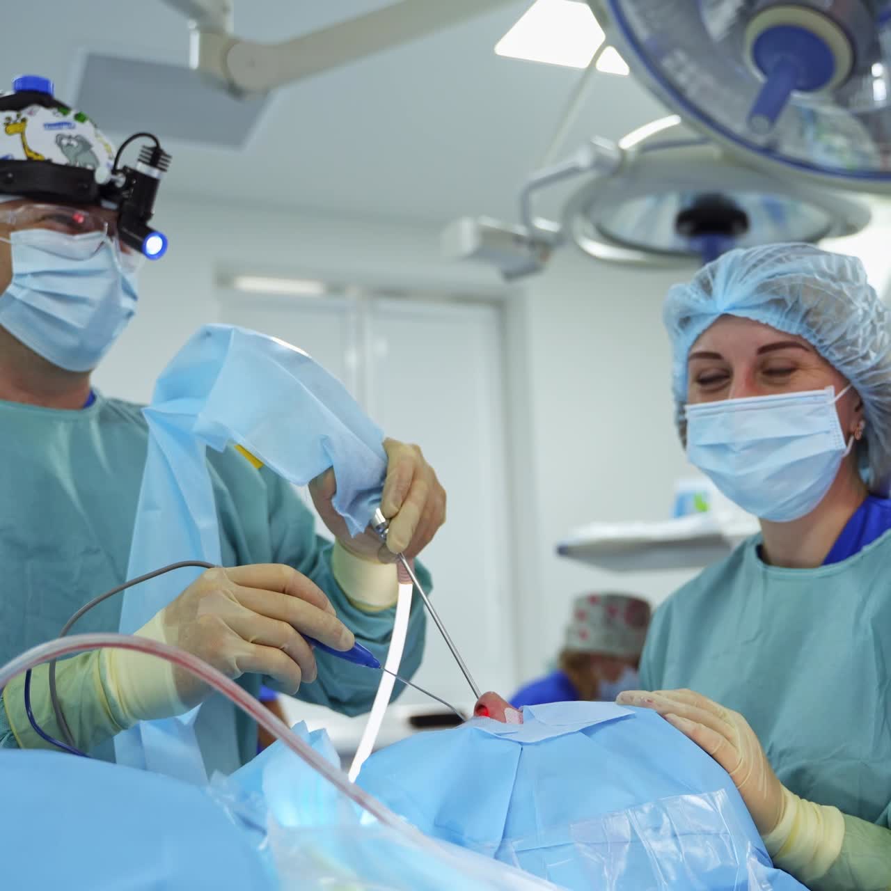Concentrated doctor applies tools in operation looking at screen in front of him. Female assistant stands beside the patient