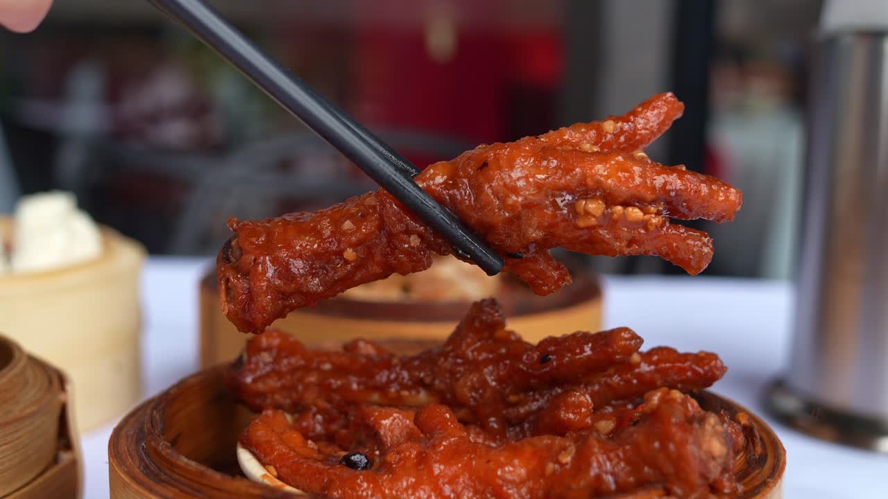 Close up shot of a traditional dim sum dish, featuring braised chicken feet in rich and spicy fermented black bean sauce, served in bamboo steamer at the restaurant, picked up using chopsticks.