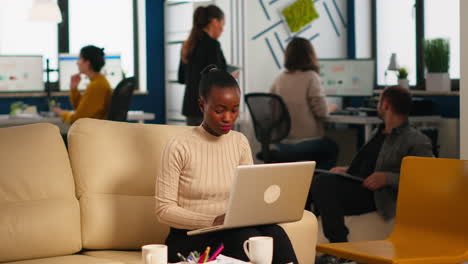 Señora-Afroamericana-Escribiendo-En-Una-Computadora-Portátil-Mirando-A-La-Cámara-Sonriendo