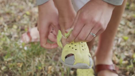 woman helping young boy put sandal shoes on in warm summer grass in slow motion